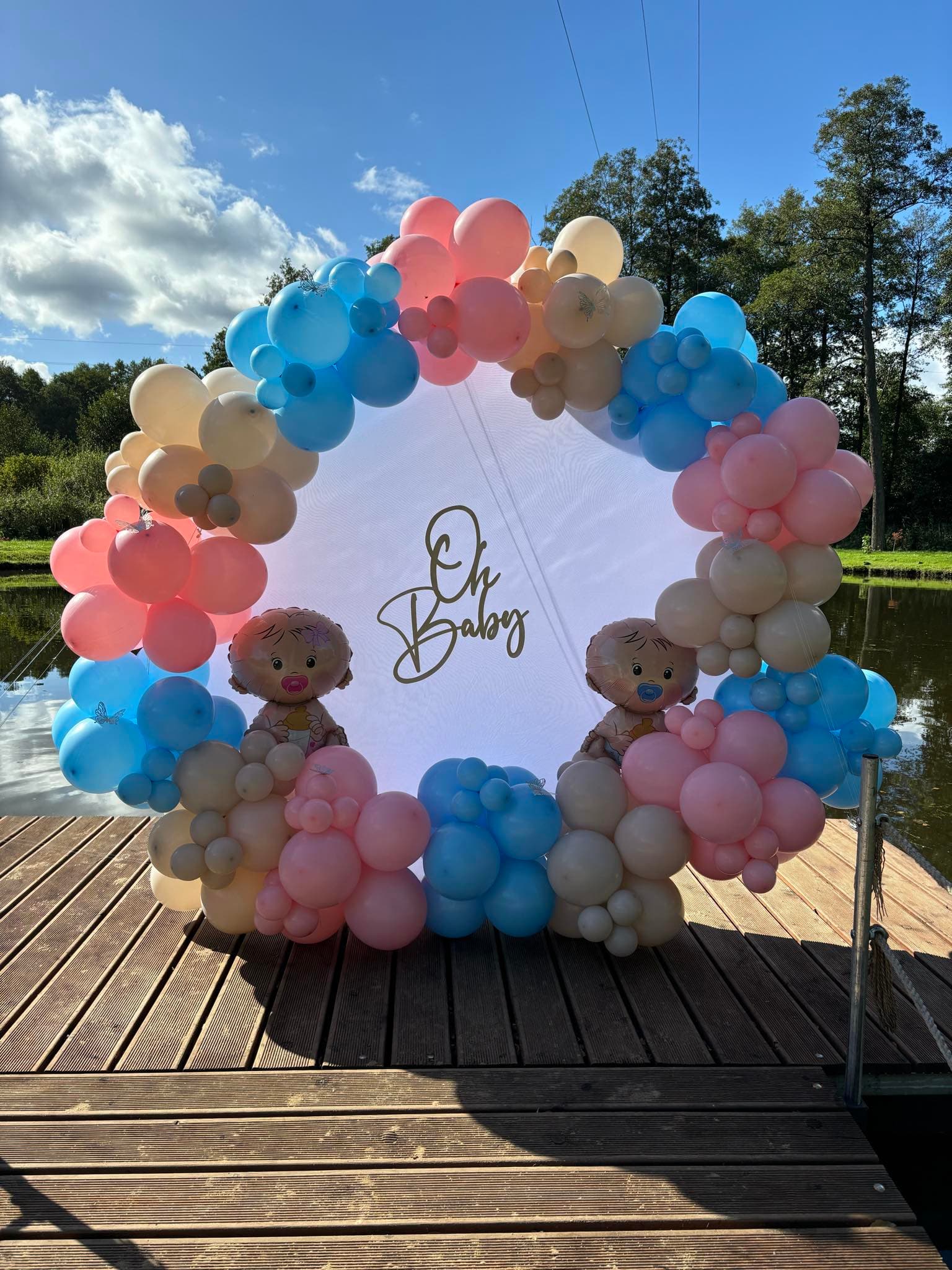 Zbliżenie na balonowe koło z napisem „Oh Baby”, dwiema maskotkami niemowląt i motylkami wśród balonów